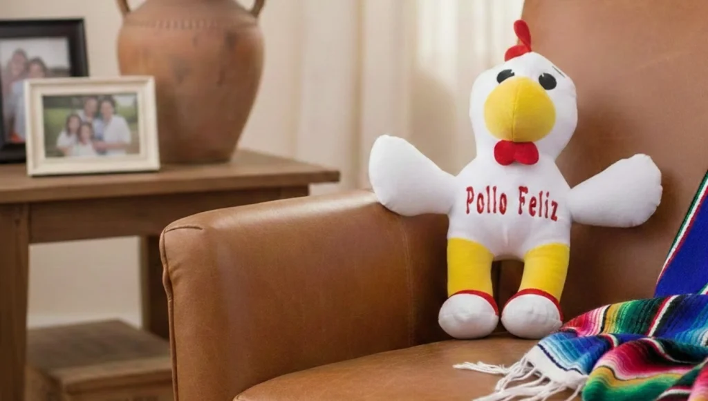 Peluche de colección Pollo Feliz apoyado en un sofá de piel marrón en una sala decorada con estilo mexicano, flores rosas y un sarape colorido.